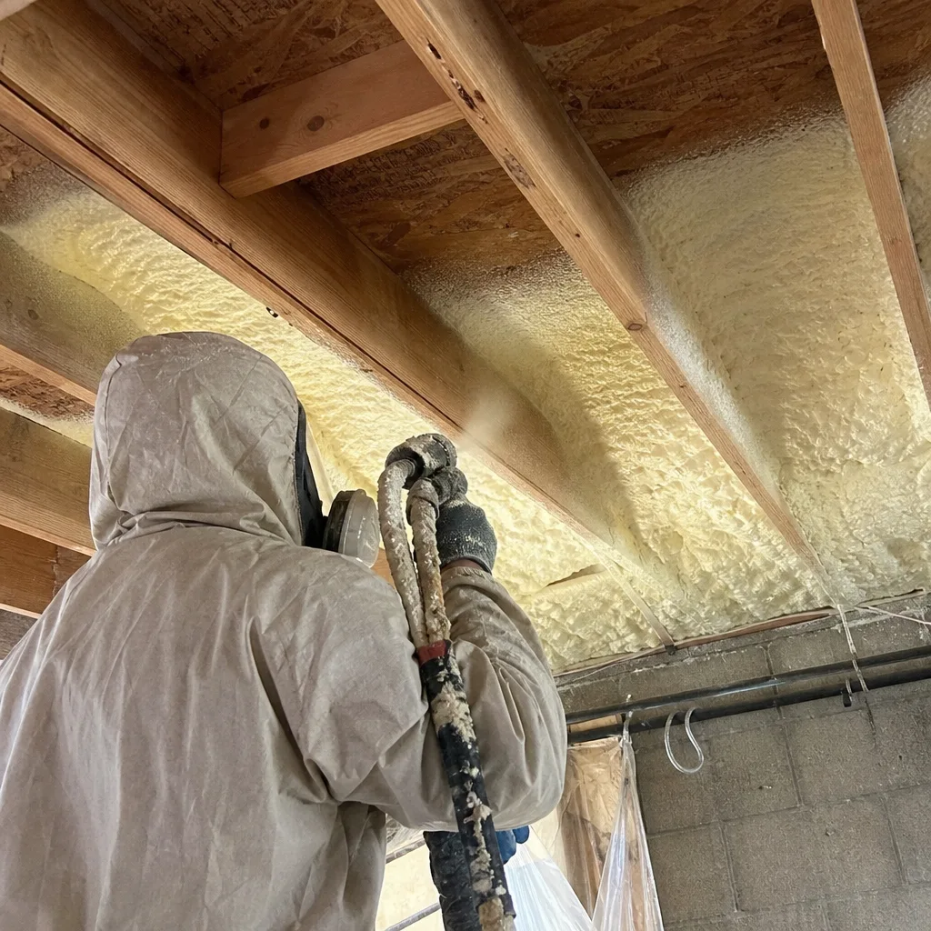 Technician applying spray foam insulation to ceiling joists
